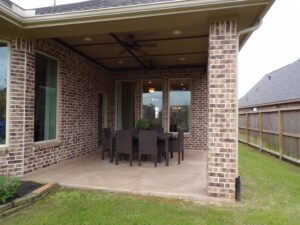 Covered patio area with a dining table set, surrounded by brick walls built by Texas builders and overlooking a lawn.