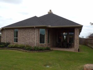 A single-story brick house crafted by Texas builders with a covered patio and lawn under a cloudy sky.