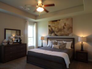 A bedroom with a bed, dresser and a ceiling fan built by Texas builders.