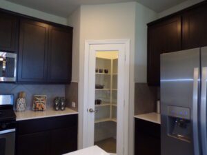 A kitchen with a refrigerator and a door to a pantry built by Texas builders.