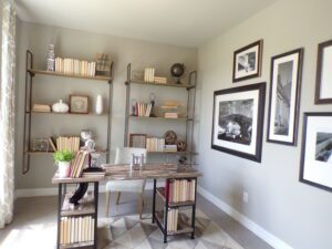 A home office with a desk, bookshelves and framed pictures designed and built by Texas builders.