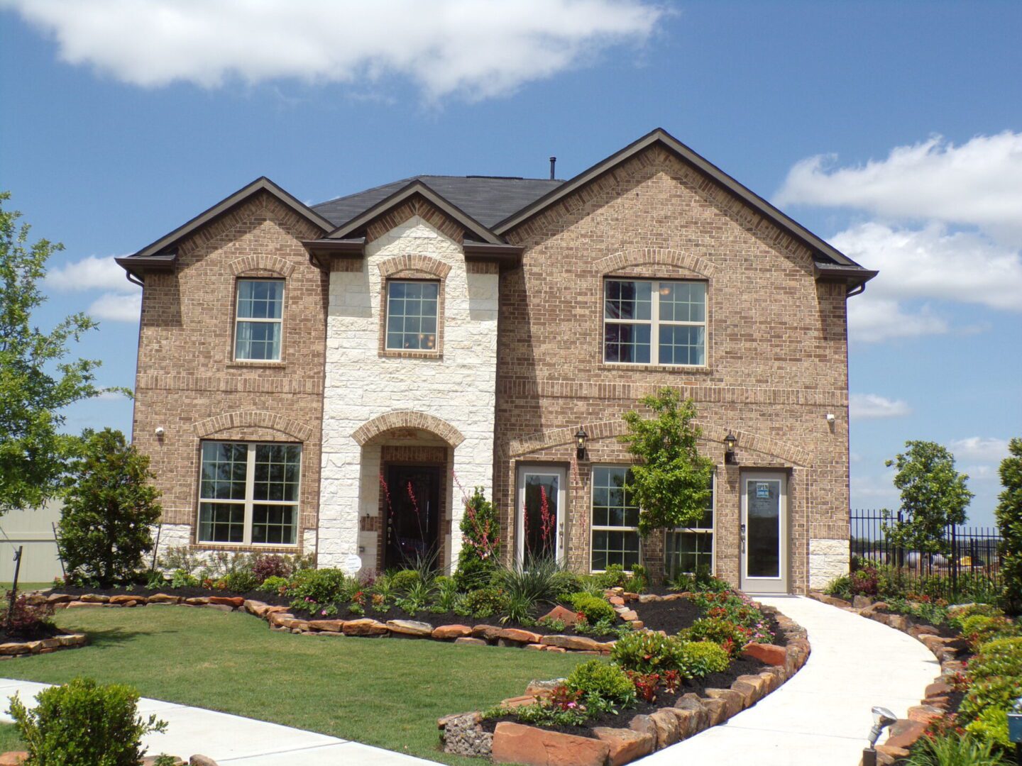 A large brick house built by Texas builders, with a lawn in front of it.