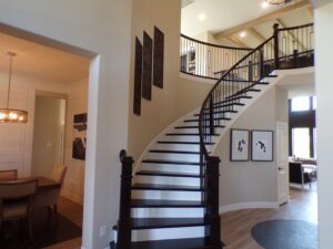 Interior of a house featuring a curved staircase with a dark wood banister and iron balusters, leading to an upper level; artwork decorates the adjoining walls, reflecting the craftsmanship of Texas builders.