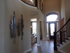 Interior of a home featuring a curved staircase with wooden rails, art on the wall, and a view towards the front door with sunlight entering, constructed by Texas builders.