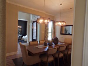 Modern dining room featuring a wooden table with beige chairs, cylindrical chandelier, and an open doorway leading to the adjacent room, designed by Texas builders.