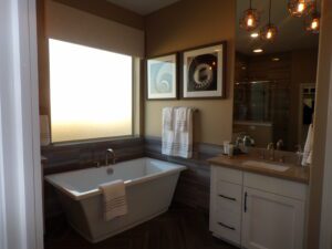 Modern bathroom interior featuring a freestanding bathtub, dual sink vanity, framed artwork, and geometric light fixtures designed by Texas builders.