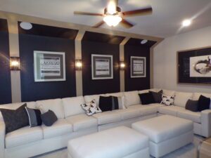 A modern living room with black striped walls, a white sectional sofa, decorative pillows, geometric artworks by Texas builders, and a ceiling fan.