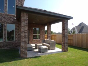 A brick house with a small patio furnished with a grey sofa set, surrounded by a wooden fence constructed by Texas builders under a clear sky.