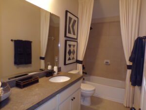 A well-lit bathroom crafted by Texas builders featuring a sink with countertop, mirror, toilet, and shower curtain with geometric patterns. Towels and toiletries are neatly arranged.