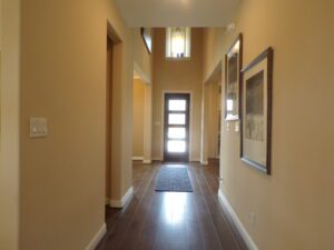 Narrow hallway in a house built by Texas builders, with beige walls, a wooden floor, framed artwork, and a door with glass panels letting in natural light.