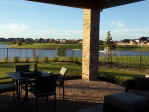 Patio with a dining table and chairs overlooking a tranquil lake and distant residential neighborhood crafted by Texas builders during sunset.