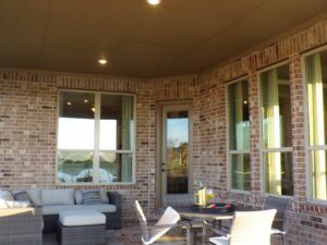 Brick house patio with comfortable seating and large windows, crafted by Texas builders, under a covered ceiling on a sunny day.