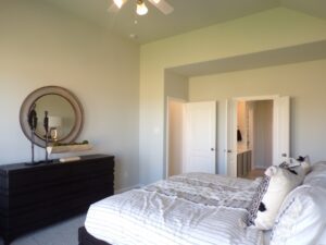 A bedroom with a bed, dresser and ceiling fan built by Texas builders.