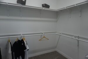 A walk in closet with clothes hanging on racks built by Texas builders.