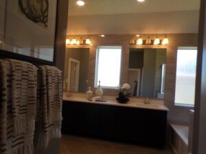 A modern bathroom interior crafted by Texas builders, featuring dual sinks, a large mirror, and pendant lighting. The decor includes striped towels and a small vase of flowers.