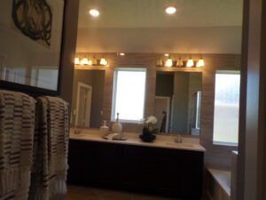 Modern bathroom with dual sinks, large mirror, and frosted glass window. Neutral tones and decorative light fixtures are visible, designed by Texas builders.