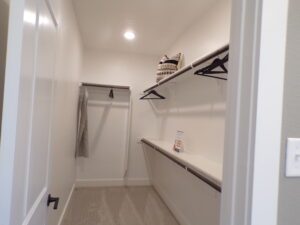 A small, tidy closet with white walls, shelves holding a basket, and a carpeted floor designed by Texas builders.