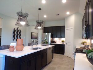 Modern kitchen interior featuring black cabinetry, a central island with a sink, and stylish pendant lights, crafted by Texas builders in a clean, well-lit space.