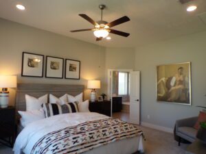 A modern bedroom featuring a double bed with geometric-patterned linens, flanked by nightstands with lamps, a ceiling fan above, and framed artwork on the walls, all expertly crafted by Texas
