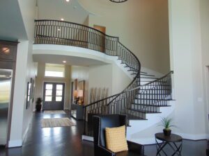 A curved staircase with black railings inside a modern home with high ceilings and light walls, crafted by Texas builders.