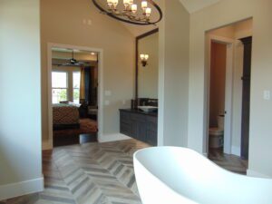 Interior view of a bathroom crafted by Texas builders, featuring a freestanding tub, herringbone tile floor, leading to a bedroom and secondary room through arched doorways.