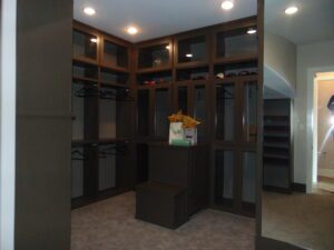 An empty walk-in closet with built-in dark wooden shelving, hanging rods, and storage boxes on the carpeted floor, constructed by Texas builders.
