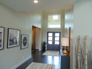 A well-lit entryway designed by Texas builders, featuring a modern front door with windows, flanked by artwork and decorative elements on the walls and floor.