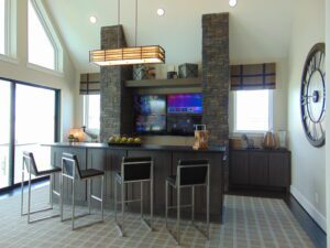 Modern kitchen with a stone island featuring bar seating and built-in TV, pendant lighting, and large windows designed by Texas builders.
