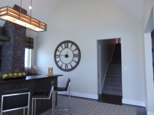 Modern kitchen with large wall clock, geometric floor tiles, a stone column, breakfast bar with stools designed by Texas builders, and pendant lighting.