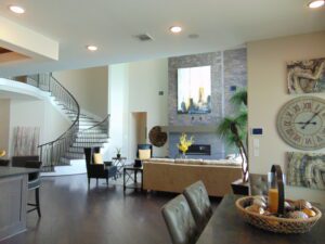 Modern living room with dark hardwood floors, a beige sofa, spiral staircase installed by Texas builders, and decorative wall elements including a large clock and stone accent wall.