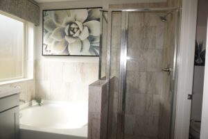 Modern bathroom with a large floral artwork above a bathtub and an adjacent glass-enclosed shower area, constructed by Texas builders.