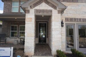 Entrance of a modern house with a stone and brick façade, featuring a covered entryway and a glass door, constructed by Texas builders.