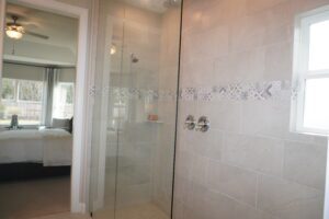 Glass shower enclosure with decorative tile work in a bathroom leading to a bedroom visible in the background, crafted by Texas builders.
