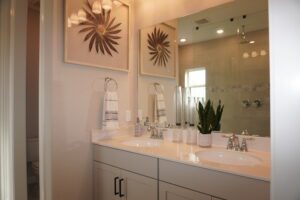 Modern bathroom interior with double vanity sinks, large mirror, white cabinets, decorative botanical artwork, and designed by Texas builders.