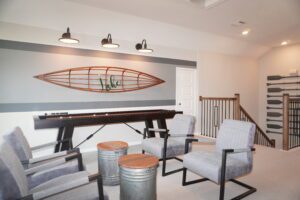 A modern home office with a large desk, metal stools, gray armchairs, and decorative wall art featuring a canoe designed by Texas builders.