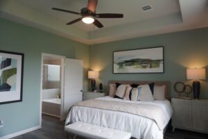 Modern bedroom designed by Texas builders, featuring a queen-sized bed with blue and white bedding, mint green walls, two side tables with lamps, wall art, and a ceiling fan.