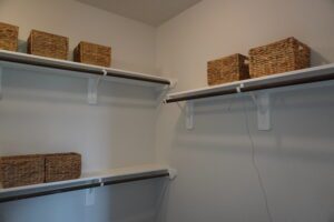 A clean, organized closet with white shelves holding several wicker baskets constructed by Texas builders.