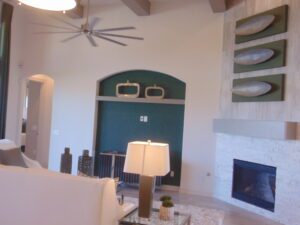 Modern living room with teak shelves on a green accent wall, white fireplace, ceiling fan, and chic decor by Texas builders.