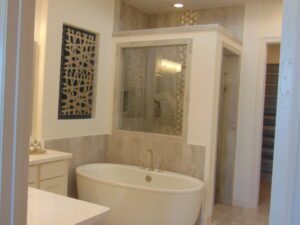 Modern bathroom with a freestanding bathtub, enclosed shower, and wall art, featuring neutral tones and tiled floors, crafted by Texas builders.