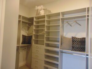 A well-organized walk-in closet designed by Texas builders featuring shelves, drawers, and seating areas with decorative pillows.