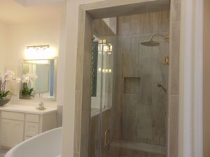 Modern bathroom featuring a walk-in shower with glass doors, gray tiled walls, and a white vanity with a mirror, crafted by Texas builders.