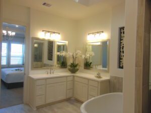 Modern bathroom with dual vanities, white cabinets, and a freestanding tub, designed by Texas builders, featuring mirrors, sconce lighting, and a decorative floral arrangement.