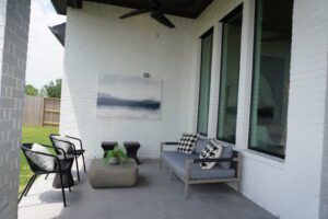 A patio with a white brick wall built by Texas builders and adorned with gray furniture.