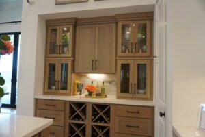 A kitchenette designed by Texas builders, featuring wooden cabinets with glass doors, a marble backsplash, and a built-in wine rack.
