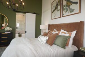 Elegant bedroom featuring a large bed with white bedding and multiple pillows, a brown headboard crafted by Texas builders, green walls, and artwork above the bed.