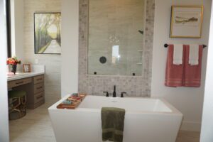 Modern bathroom featuring a freestanding bathtub, beige tile walls, and a vanity area, decorated with framed art and red towels, designed by Texas builders.