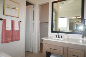 Modern bathroom with a large mirror, wooden vanity, and hanging terracotta towels. Another bathroom visible through the open door, showcasing the expertise of Texas builders.
