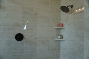 Modern bathroom with beige tiles, crafted by Texas builders, featuring a wall-mounted rainfall showerhead, built-in shelves with toiletries, and subtle lighting.