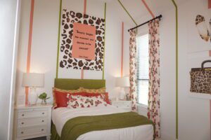 A stylish bedroom with leopard print and green accents, featuring a framed quote on the wall, and patterned curtains, designed by Texas builders.