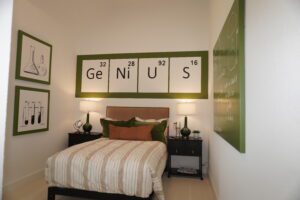 A well-decorated bedroom with a "genius" banner above the bed, striped bedding, and science-themed art on the walls, designed by Texas builders.